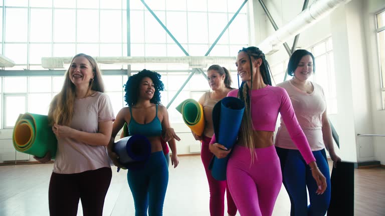 Women of different body shapes leave gym holding sports mats