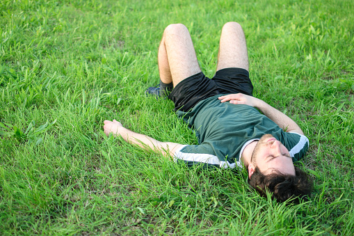 Image of young man with green t-shirt lying on grass in park after exercising exhausted