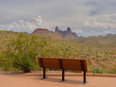 A view of the desert in Big Bend. A park bench on a canyon rim with views of the the Mule's Ears formation in Big Bend. Storm clouds gather on the horizon.