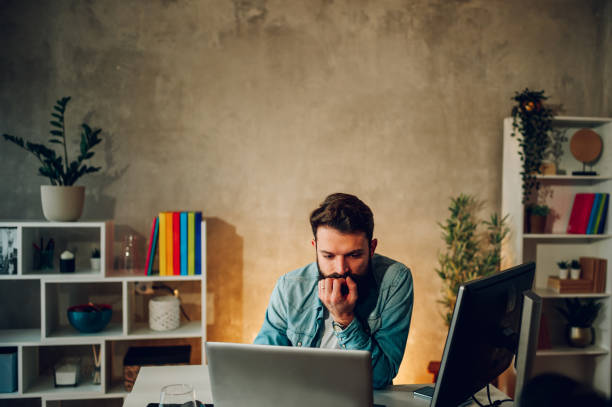 istock A focused bearded software engineer is sitting at his home office, looking at the laptop and solving problems in code. 1494922236