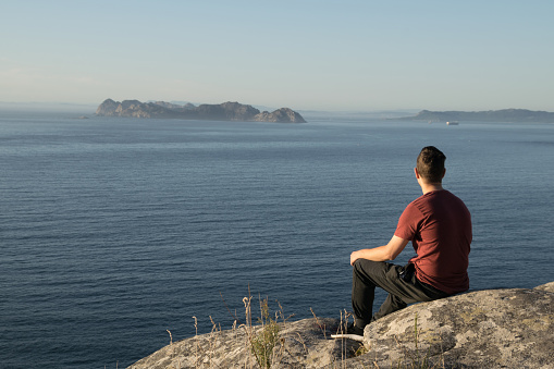 Young man sitting on the rocks looking at the horizon