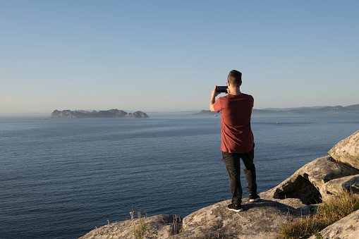 Rear view of a Young man taking a photo of the sea from the mountain