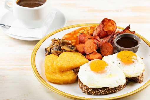 Fried eggs with sausages, nuggets, mushrooms and cup of coffee. Îreakfast concept.