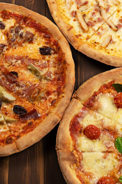 istock Three different pizzas on wooden background with tomato sauce, mixed cheese selection, ham and pork gyros. 1494924797