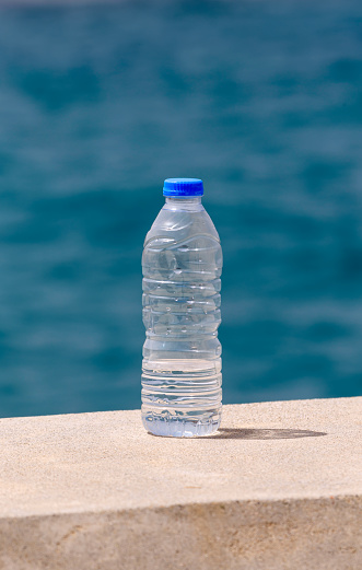 The concept of thirst. A bottle of water stands against the background of the sea on a sunny day close-up