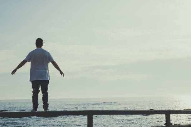 istock Man with outstretched arms standing on a railing looking at the ocean 1494928069