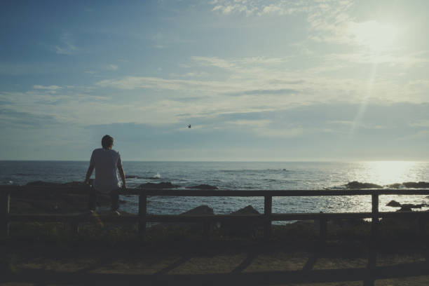 istock Boy sitting on a railing watching the ocean at sunset 1494928077