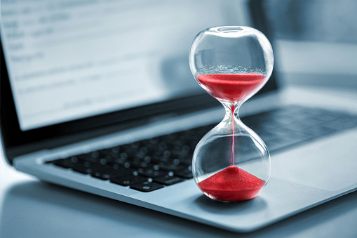 Hourglass with red sand stands on the laptop computer - time management concept