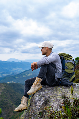 Young Latino outdoorsman sitting on top of a mountain, hiking in the mountains of Colombia, lifestyle, travel and adventure concept.