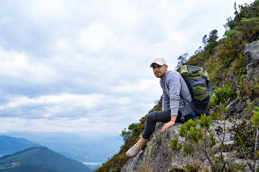 Young Latino outdoorsman sitting on top of a mountain, hiking in the mountains of Colombia, lifestyle, travel and adventure concept.