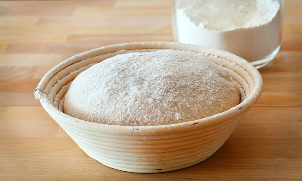Dough rising in the proofing basket on a wooden table stock photo