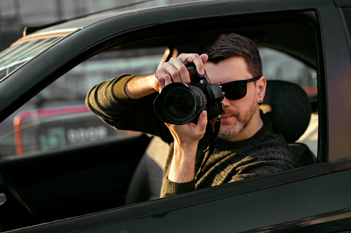 Man detective or agent taking photos from the car, wearing modern sunglasses