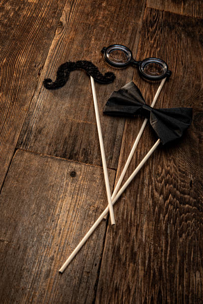 This is a photograph of a bowtie, glasses and mustache on a stick all sitting on an old Wood retro background. There are no people in the photograph