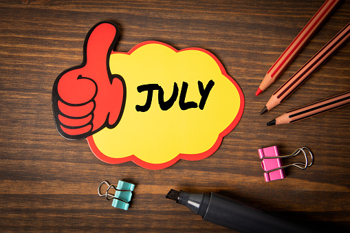 JULY. Sticky note with text on a wooden background.