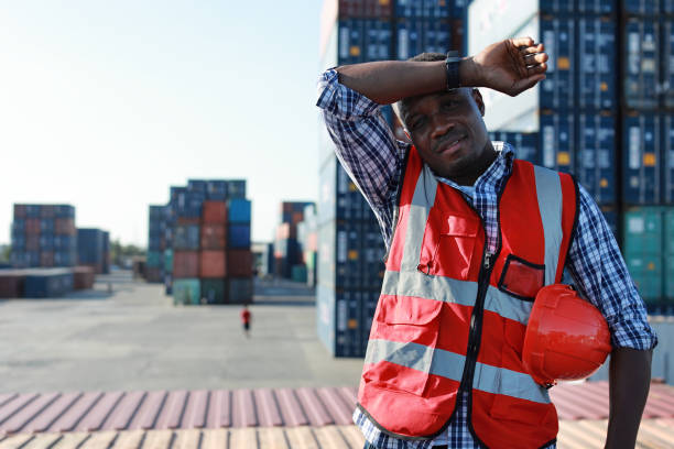 istock Foreman engineer man standing and holding hard hat while wipe the sweat away. Confident engineering work at container cargo site and checking industrial container cargo freight ship 1494967179