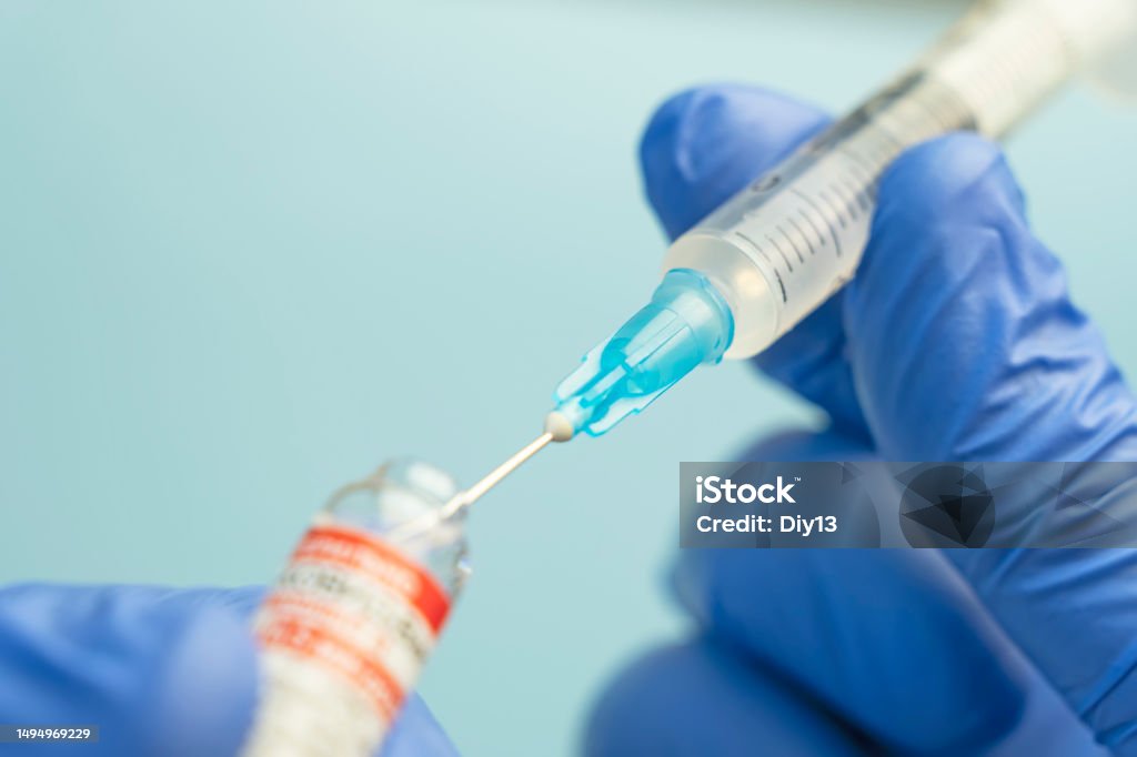 Macro of a hypodermic syringe or needle being filled with mRNA vaccine from bottle against blue background Macro of a hypodermic syringe or needle being filled with mRNA vaccine from bottle against a blue background Addiction Stock Photo