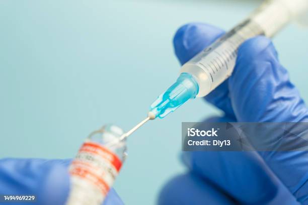 Macro Of A Hypodermic Syringe Or Needle Being Filled With Mrna Vaccine From Bottle Against Blue Background Stock Photo - Download Image Now