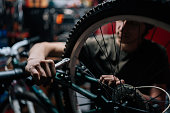 Detail close-up of unrecognizable repairman repairing mountain bike using special tool working in bicycle repair shop with dark interior.