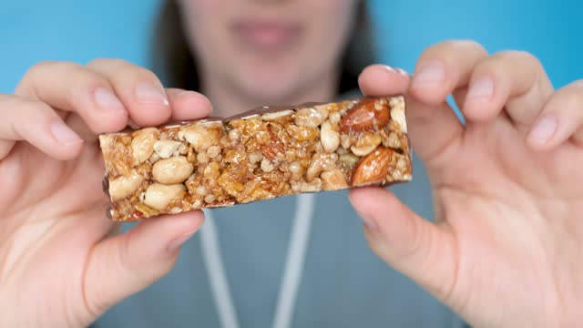 Young woman holding protein bar on blue background, selective focus.