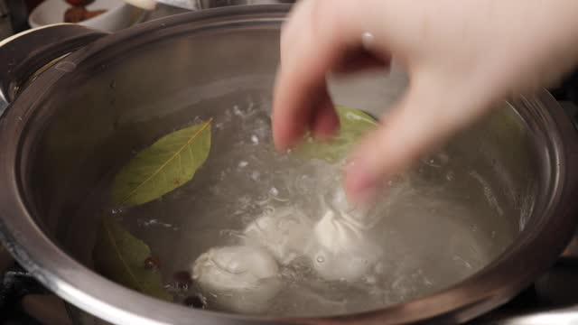 Boiling water in a saucepan with black and allspice peas, dried bay leaf. The girl throws dumplings into the boiling water.