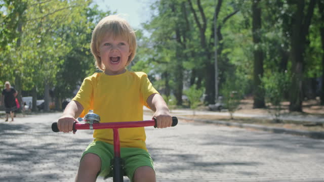 Joyful child in bright clothes rides tricycle along track