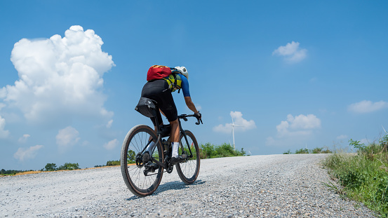 Asian man rides a bicycle gravel road in a field of wind turbines.