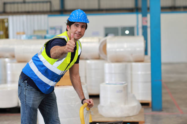 istock Warehouse worker pulling a pallet truck and taking or upload package box to shelf in large warehouse. Active caucasian man showing thump up and looking at camera with smiling. 1494988453