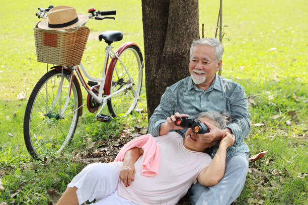 Portrait of happy asian senior man and woman lying on lap and embracing with bicycle and hat in summer garden outdoor. Lover couple going to picnic at the park. Happiness marriage lifestyle concept. retrato de un hombre y una mujer mayores asiáticos felices acostados en el regazo y abrazándose con bicicleta y sombrero en el jardín de verano al aire libre. pareja de amantes que van de picnic al parque. concepto de estilo de vida de matrimonio de fel