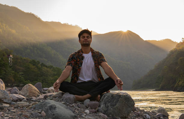 Young man meditating on rocks at lakeshore during vacation