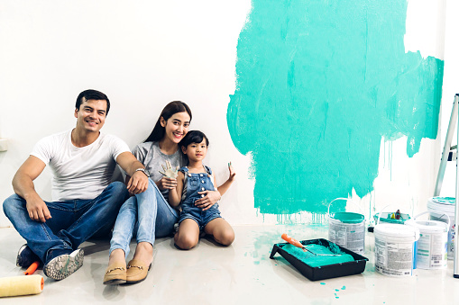 Happy family using a paint roller and painting walls in their new home