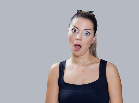 Portrait of real woman making a surprised face expression over gray background, studio shot