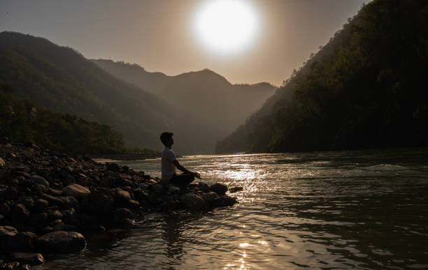 Young man meditating on rocks at lakeshore during vacation