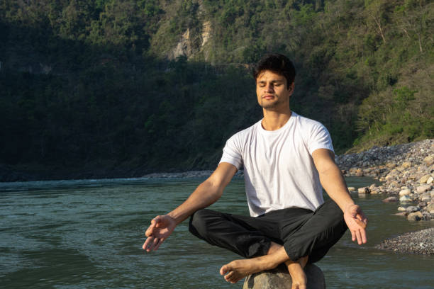 istock Young man meditating on rocks at lakeshore during vacation 1494999324
