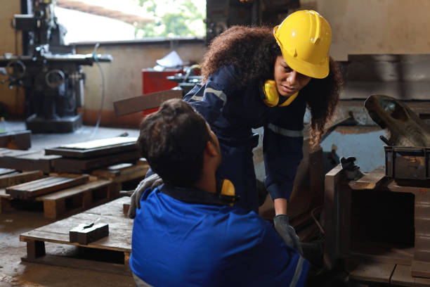 istock Young technician engineer or worker man in protective uniform had a leg accident lying on the floor in metal lathe factory. Safety colleague team helping him from accident. First aid training concept 1495000784
