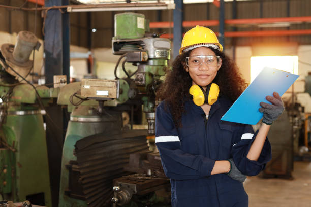 istock Technician engineer woman in protective uniform with clipboard and looking camera while maintenance operation or check lathe metal machine at heavy industry manufacturing factory. Metalworking concept 1495000991