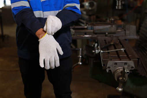Technician engineer man hands in protective uniform maintenance operation or checking lathe metal machine while putting on engineer gloves at heavy industry manufacturing factory. Metalworking concept