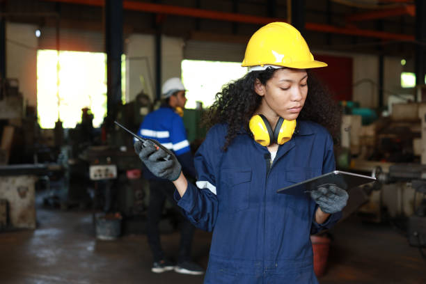 istock Technician engineer or worker woman in protective suit using walkie talkie radio with tablet while controlling or maintenance operation work lathe metal machine at heavy industry manufacturing factory 1495001373