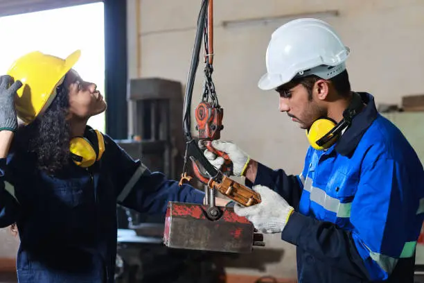 Photo of Teamwork technician engineer or worker in protective uniform with safety hardhat standing and maintenance operation or checking overhead crane remote control at heavy industry manufacturing factory