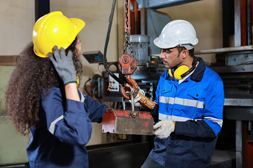 Teamwork technician engineer or worker in protective uniform with safety hardhat standing and maintenance operation or checking overhead crane remote control at heavy industry manufacturing factory