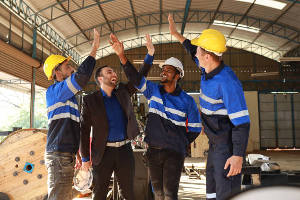 istock Group of technician engineer and businessman in protective uniform with hardhat standing and raising hands celebrate successful together or completed deal commitment at metal lathe factory industry 1495002512