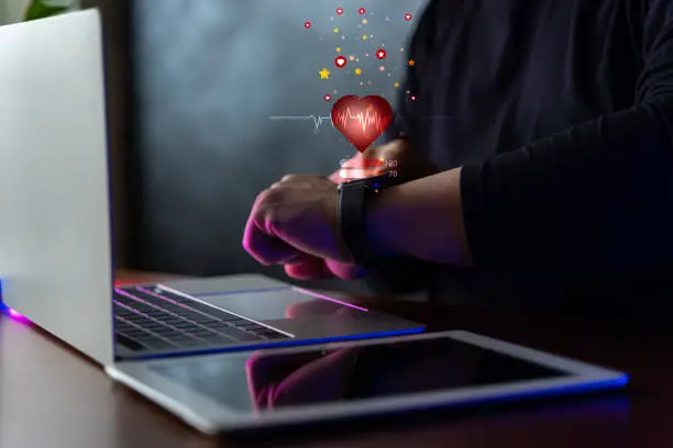 Photo of Man using smart watch technology checking heart rate with health app icon on the screen. Holographic icon user interface.