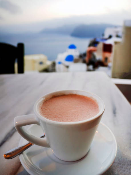 istock High angle view a cup of hot chocolate or cacao in the white cup on marble table with blurry of Santorini island view in the background, Greece 1495005461