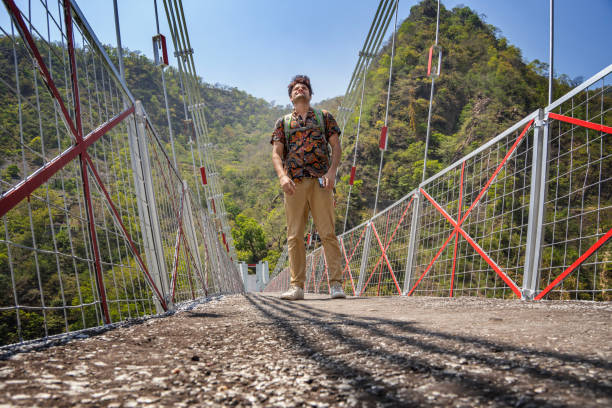istock Cheerful male explorer standing on footbridge against lush mountain 1495013561