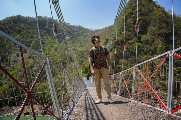 istock Cheerful male explorer standing on footbridge against lush mountain 1495014192