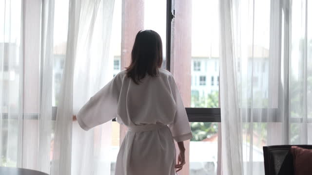Indonesian Young Female Traveller Opening Curtain Window in Hotel Room