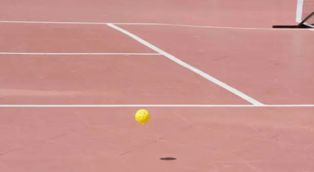 Photo of bouncing ball on a red pickle ball court with the kitchen in background horizontal