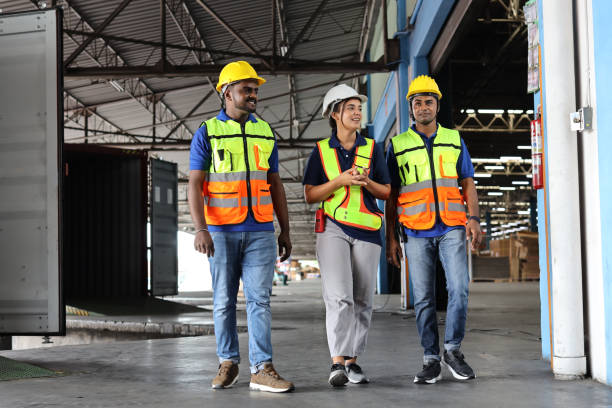 istock Group of warehouse workers with hardhats and reflective jackets using tablet, walkie talkie radio and cardboard while controlling stock and inventory in retail warehouse logistics, distribution center 1495015169