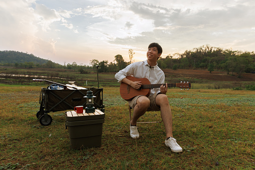 Young Asian man playing guitar on the ground camp
