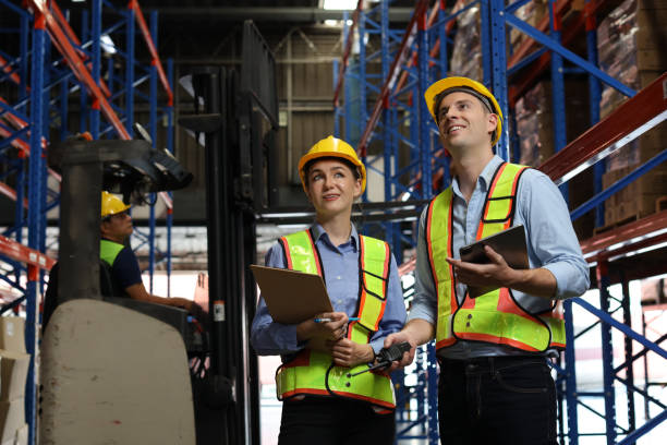 istock Group of warehouse workers with hardhats and reflective jackets using tablet, walkie talkie radio and cardboard while controlling stock and inventory in retail warehouse logistics, distribution center 1495016197