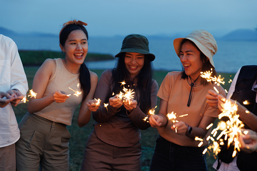 Group of People Friends Asian men and women playing sparklers dance on the ground Camping,